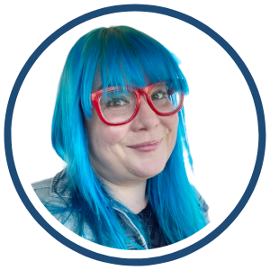 KellyMarie Meek Headshot of KellyMari Meek, smiling with long blue hair, red glasses, and a denim jacket, shown inside a circular blue border.