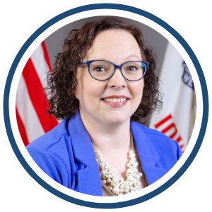 Shannon Grundmeier – Iowa Department of Education Headshot of Shannon Grundmeier smiling and wearing a bright blue blazer, glasses, and a pearl necklace, against a neutral background.